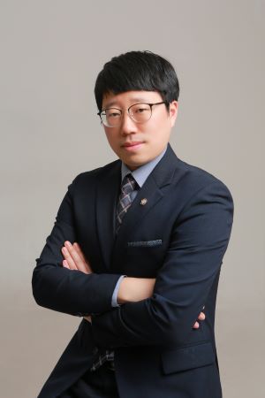 Professional portrait of a man in a navy suit with glasses, arms crossed, looking at the camera.