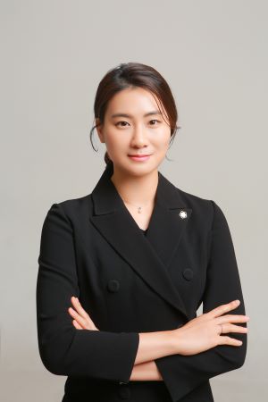 Professional woman in a black blazer standing with arms crossed against a neutral light background.