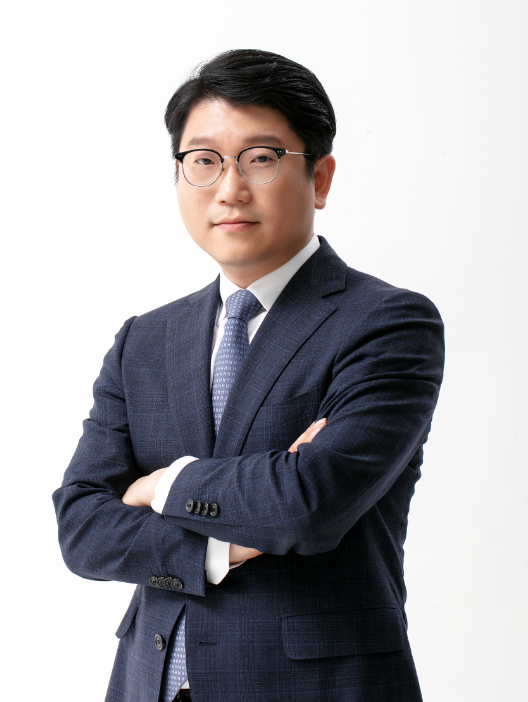 Professional man in a dark blue suit and glasses, arms crossed, looking at the camera against a white background.