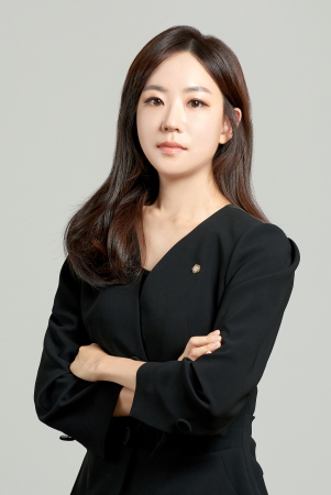 Professional-looking woman with arms crossed, wearing a black blazer against a neutral background