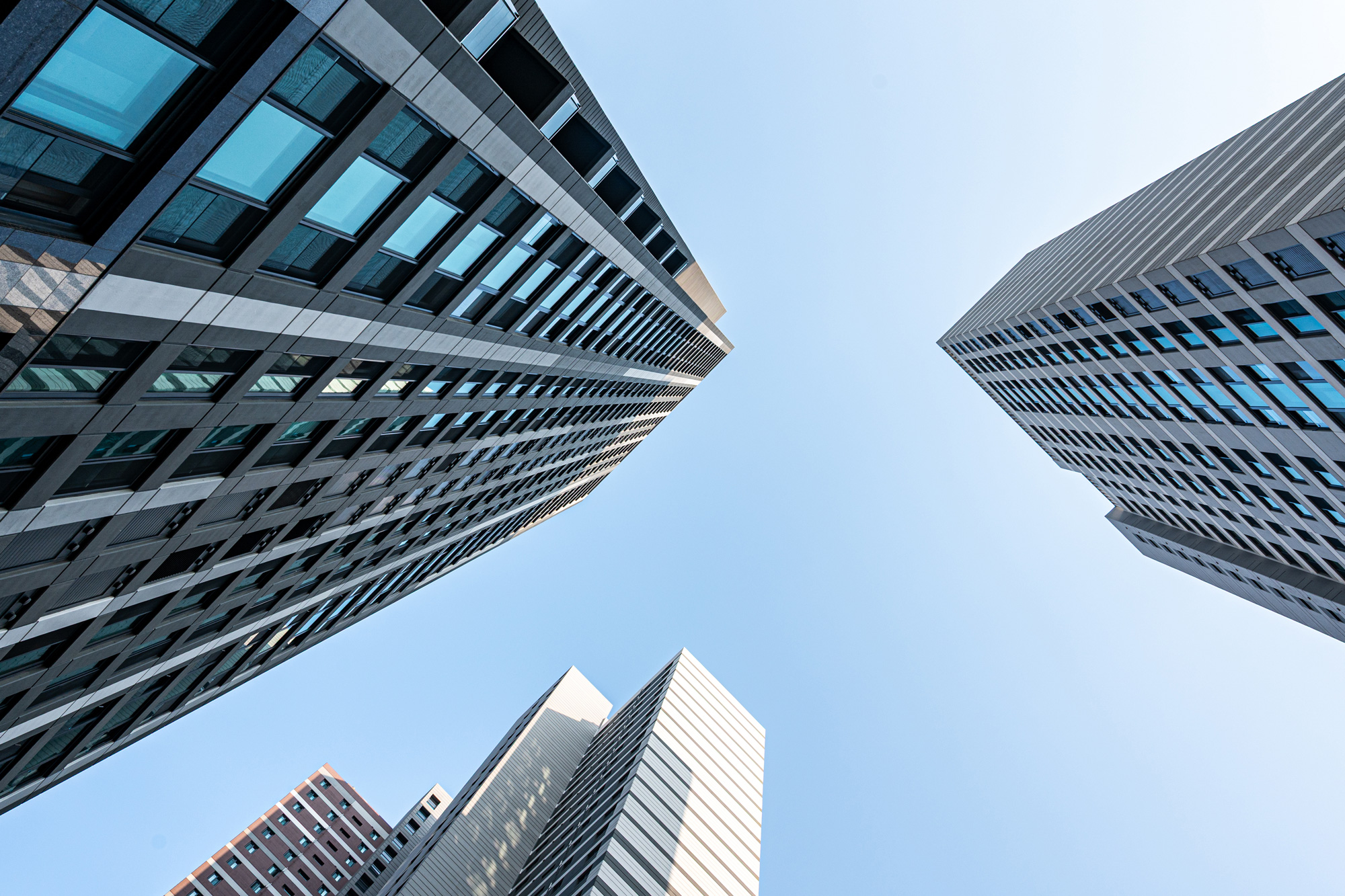 Low-angle view of tall modern office buildings converging toward a clear blue sky.