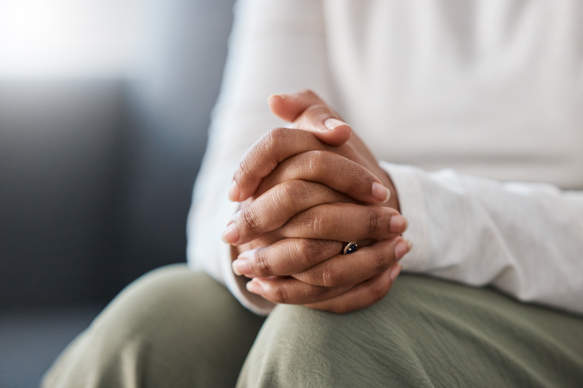 Close-up of hands folded in the lap, showing a dark-stone ring on one finger.